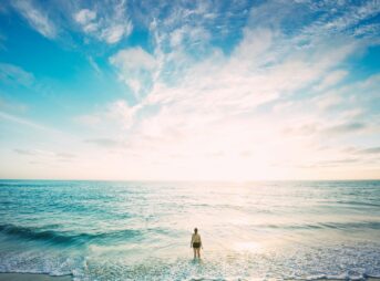 woman on sea in front of sun